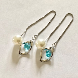 May include: A pair of silver dangle earrings with a pearl and a blue crystal on each earring.