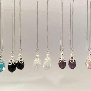 Puede incluir: Una colección de pendientes colgantes con cadenas plateadas y cuentas decorativas en forma de lágrima en varios colores, incluyendo azul, negro, transparente, morado y rosa. Los pendientes tienen un diseño delicado y femenino.