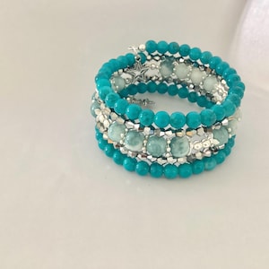 May include: A multi-strand wrap bracelet featuring turquoise-coloured beads, pale green marbled beads, and faceted silver-toned metallic spacers. The design includes a small silver-toned star charm attached to the top strand of the bracelet.