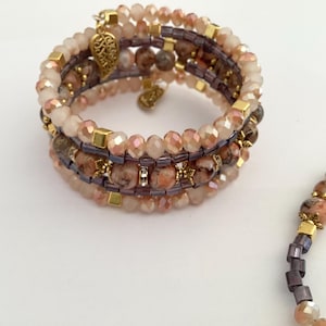 May include: A multi-strand beaded bracelet with a matching necklace. The bracelet features a mix of peach, brown, and gold beads, with gold-colored accents and a decorative charm. The necklace has similar beads. The jewelry is set against a white background.