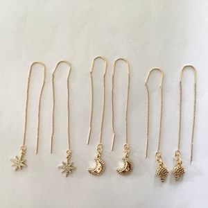 Puede incluir: Seis pares de pendientes de aro dorados con diferentes colgantes. Los colgantes incluyen una estrella, una luna creciente y una pequeña forma geométrica.