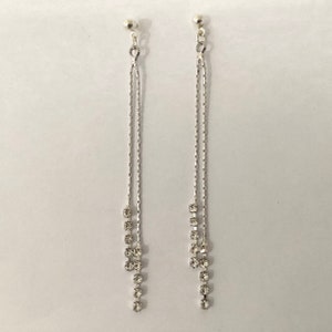 Puede incluir: Un par de pendientes de plata con diseño de cadena y detalles de cristal transparente.