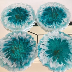 May include: Four teal and white resin coasters with a floral design. The coasters are round and have a slightly irregular edge.