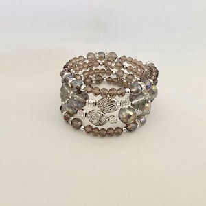 May include: A multi-strand bracelet with brown and gray glass beads and silver tone metal accents. The bracelet is made of multiple strands of beads that are wrapped around the wrist.
