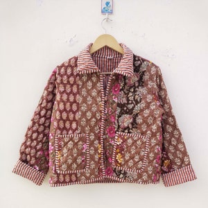 May include: A quilted jacket with a patchwork design. The jacket features floral and geometric patterns in brown, pink, and white. It has a collared neckline, two front pockets, and striped cuffs and collar trim.
