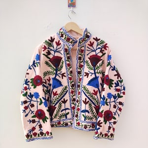 May include: A pink embroidered jacket with a floral pattern in shades of blue, green, and red. The jacket has a mandarin collar and a button closure.