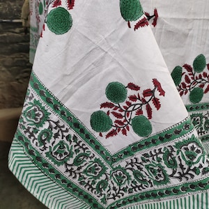 May include: White cotton tablecloth with a green and red floral print. The tablecloth has a green and white striped border.