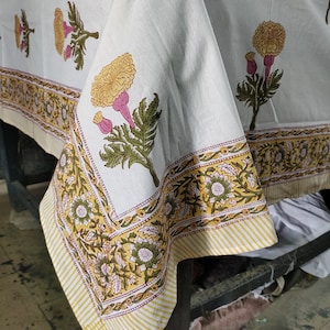 May include: White cotton tablecloth with a yellow and green floral print. The tablecloth has a yellow and white striped border with a floral design.