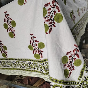 May include: White cotton fabric with a green and red floral print. The fabric has a border with a paisley design.
