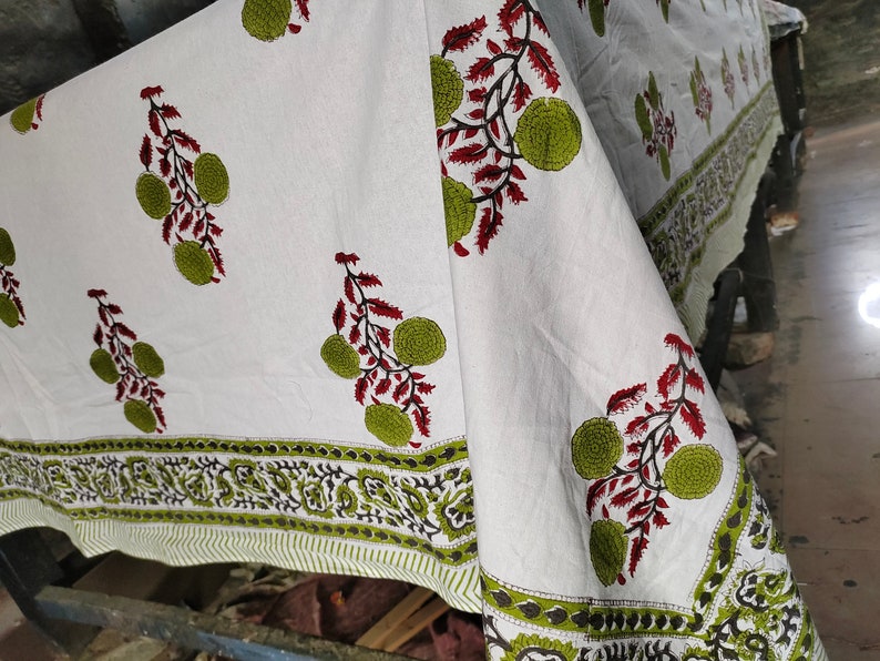 May include: White cotton fabric with a green and red floral print. The fabric has a border with a paisley design.