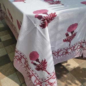 May include: White tablecloth with a repeating pattern of pink floral designs. The tablecloth has a border with a paisley and striped pattern in burgundy. The tablecloth is made of a soft, lightweight fabric.