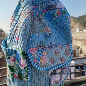 May include: A blue quilted backpack with floral patchwork. The backpack features a front pocket and adjustable straps. The design incorporates various shades of blue and floral patterns in pink, green, and white.