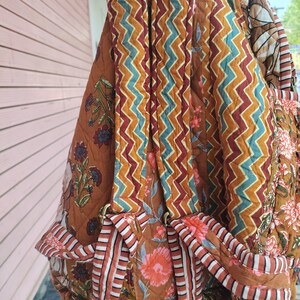 May include: Quilted backpack with a brown, orange, and teal zigzag pattern on the straps and a floral print on the body. The backpack has adjustable straps and a top handle. The bag is made of a soft, quilted fabric.
