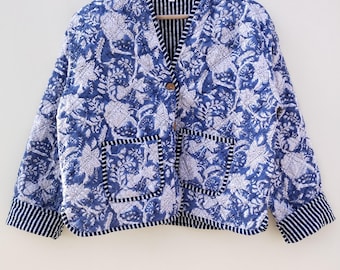 May include: A blue and white floral print jacket with two front pockets and a striped trim. The jacket is quilted and has a button closure. The jacket is hanging on a wooden hanger.