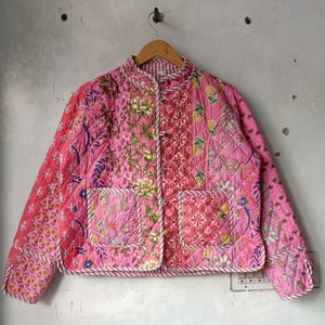 May include: A pink quilted jacket with a floral print and a button closure. The jacket is made of patchwork fabric and has a unique, bohemian style.