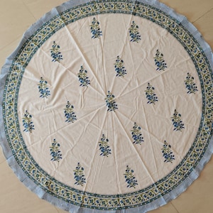 May include: A white round tablecloth with a blue and green floral print border. The tablecloth has a repeating pattern of small blue flowers with green leaves.