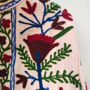 May include: A pink fabric with colorful embroidered flowers. The flowers are in shades of red, blue, green, and brown. The fabric has a textured surface.