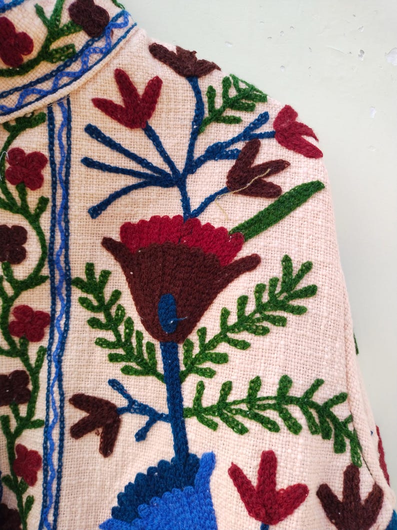 May include: A pink fabric with colorful embroidered flowers. The flowers are in shades of red, blue, green, and brown. The fabric has a textured surface.