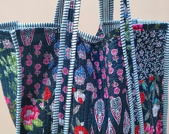 May include: A large tote bag featuring a floral design in pink, red, and blue on a dark background. The bag has striped handles and trim. The bag is quilted and appears to be made of fabric.