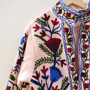 May include: A pink embroidered jacket with a high collar and floral designs in shades of blue, green, red, and brown.