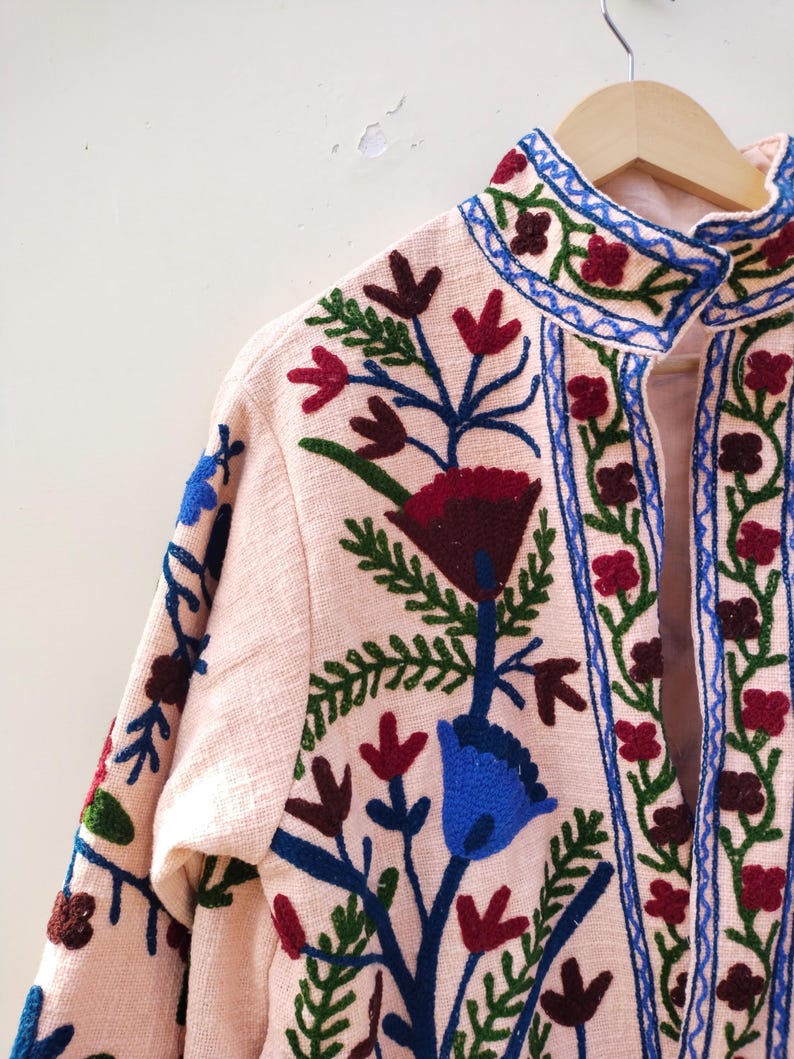 May include: A pink embroidered jacket with a high collar and floral designs in shades of blue, green, red, and brown.