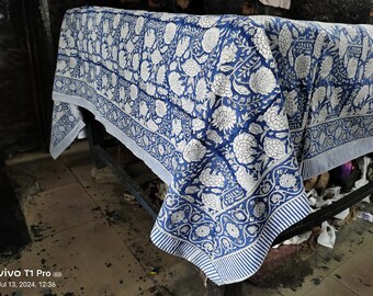 Puede incluir: Un mantel de mesa de algodón azul y blanco con un patrón floral. El mantel está doblado y drapeado sobre una mesa.