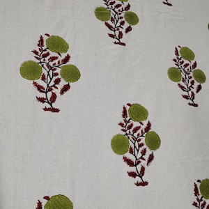 May include: White fabric with a repeating pattern of green and red floral designs. The flowers are stylized and have a circular shape.