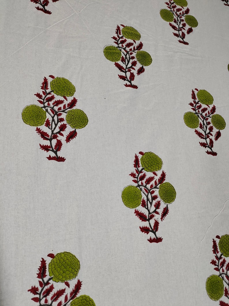 May include: White fabric with a repeating pattern of green and red floral designs. The flowers are stylized and have a circular shape.