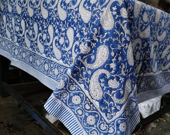 Puede incluir: Un mantel de mesa azul y blanco con estampado de paisley, borde blanco y rayas blancas. El mantel está doblado y drapeado sobre una mesa.