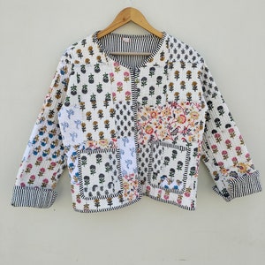 Puede incluir: Chaqueta acolchada blanca con un diseño de patchwork con estampados florales en varios colores. La chaqueta tiene cuello redondo, mangas largas y dos bolsillos delanteros. Los puños y el cuello están ribeteados con rayas blancas y negras.