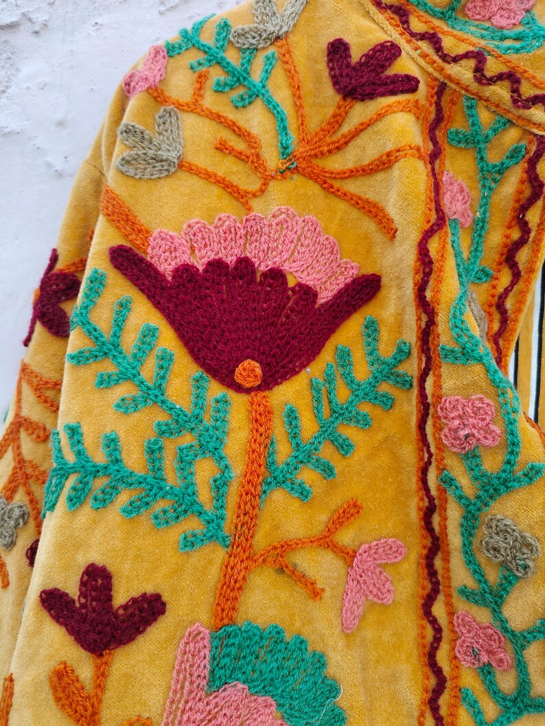May include: Mustard yellow embroidered jacket with a floral design. The jacket features a large, central flower in deep red and pink, surrounded by teal and orange embroidered leaves and stems. Additional small flowers and leaf clusters are scattered across the fabric.