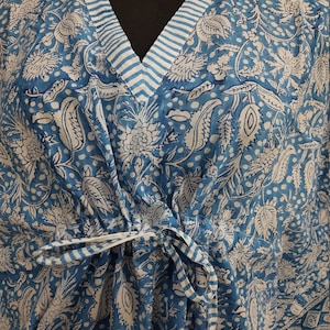 May include: A blue and white cotton kaftan with a floral print and a striped trim. The kaftan has a V-neck and a tie at the waist.