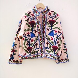 May include: A pink embroidered jacket with a floral pattern in shades of blue, green, red, and white. The jacket has a stand-up collar and a button closure.