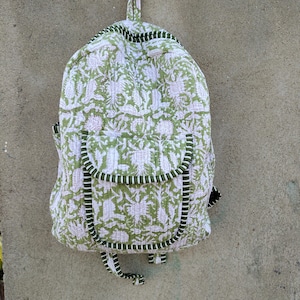 May include: A quilted backpack with a green and white floral pattern. The backpack has a rounded shape, a small top handle, and two front pockets. The edges are trimmed with a dark green and white striped fabric.