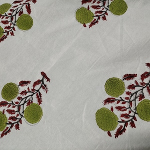 May include: White fabric with a repeating pattern of green and red floral designs. The flowers are stylized and resemble small, round buds.