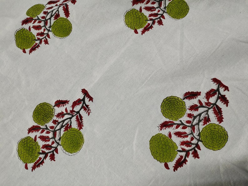 May include: White fabric with a repeating pattern of green and red floral designs. The flowers are stylized and resemble small, round buds.