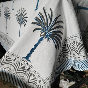May include: White cotton fabric with a blue and gray palm tree print. The fabric has a border with a geometric pattern.