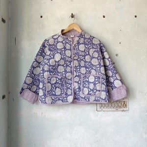Peut inclure: Une veste matelassée violette à imprimé floral blanc et col mandarin. La veste a deux poches et une fermeture à bouton.
