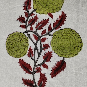 May include: A white fabric with a green and red floral print. The flowers are stylized and have a circular shape. The leaves are a deep red color.