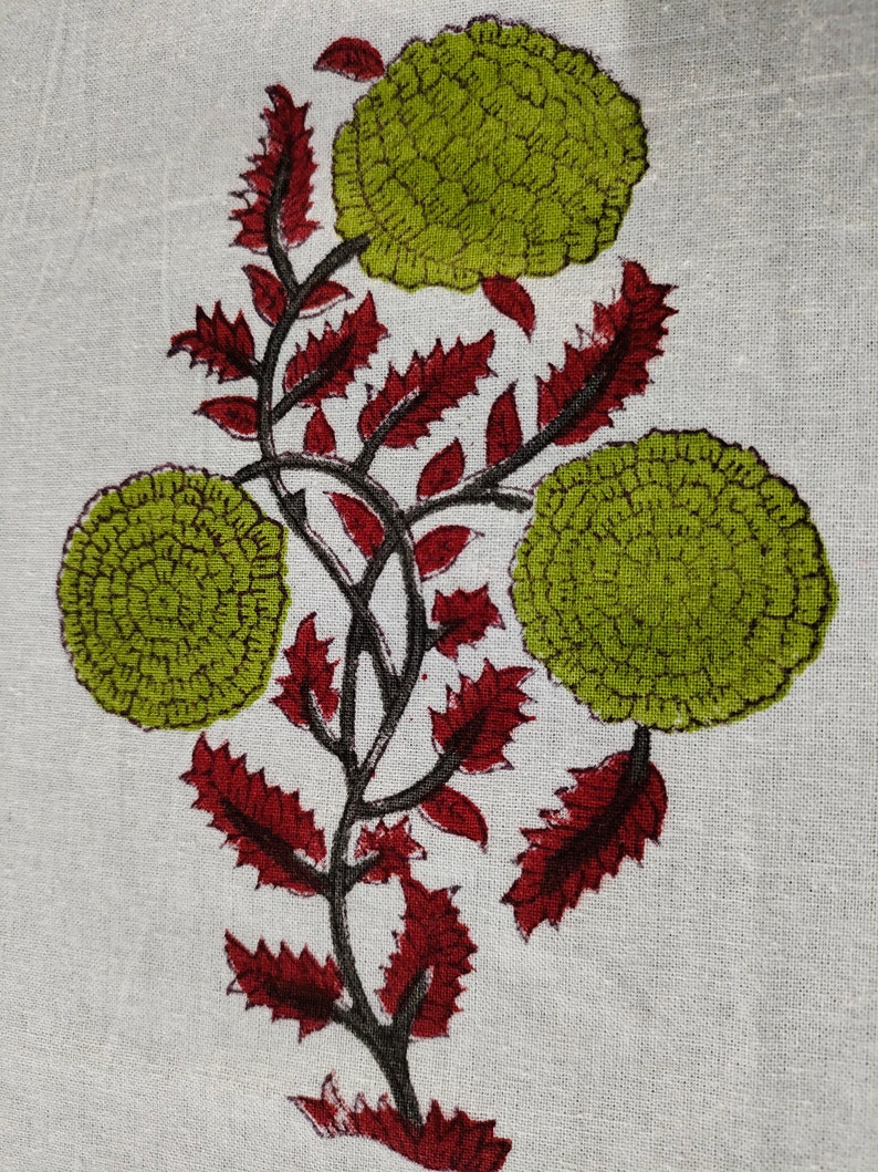 May include: A white fabric with a green and red floral print. The flowers are stylized and have a circular shape. The leaves are a deep red color.