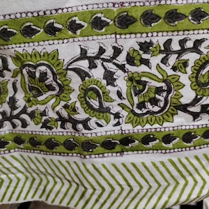 May include: White fabric with a green and black floral pattern. The pattern includes paisley shapes and leaves. The fabric has a white background with a green and black border.