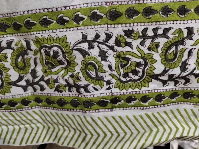 May include: White fabric with a green and black floral pattern. The pattern includes paisley shapes and leaves. The fabric has a white background with a green and black border.