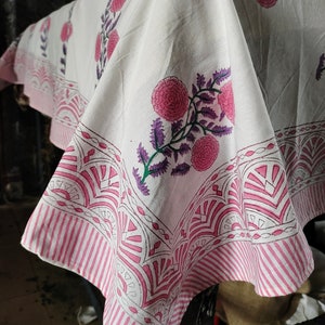 May include: White cotton fabric with a pink and purple floral print. The fabric has a pink and white striped border with a geometric design.