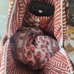 May include: Inside view of a quilted tote bag with a black phone in the pocket. The bag has a striped pattern in orange and white, with floral fabric inside. A smaller, floral-printed pouch is also visible within the bag's interior.