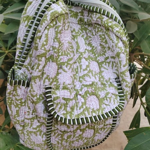 May include: A green and white floral patterned backpack with a quilted design. The backpack has two front pockets and a zipper closure. The edges are trimmed with a dark green and white striped fabric.