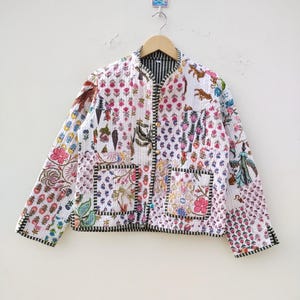 Pode incluir: Casaco acolchoado com design patchwork. O casaco apresenta um fundo branco com estampas florais e animais em várias cores. Possui gola e acabamento listrados em preto e branco, dois bolsos frontais e fecho de botões.