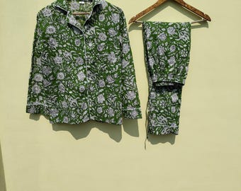 May include: A green and white floral print pyjama set with a button-up shirt and matching trousers. The set is hanging on two wooden hangers.