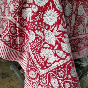 May include: Red and white cotton tablecloth with a floral print. The tablecloth has a white border with a red and white striped pattern.
