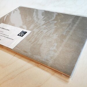 K&ouml;nnte beinhalten: Eine braune Papierkarte mit einer wei&szlig;en Visitenkarte darauf. Die Visitenkarte lautet "Chris Williams Artist" und enth&auml;lt Kontaktinformationen. Die Karte ist in durchsichtige Plastikfolie verpackt.