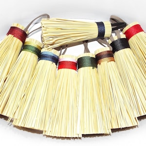 May include: A set of ten small, natural-fiber brooms with colorful ribbon ties. The brooms are made of straw and have a natural, rustic look. The ribbons are in a variety of colors, including red, blue, green, and brown.